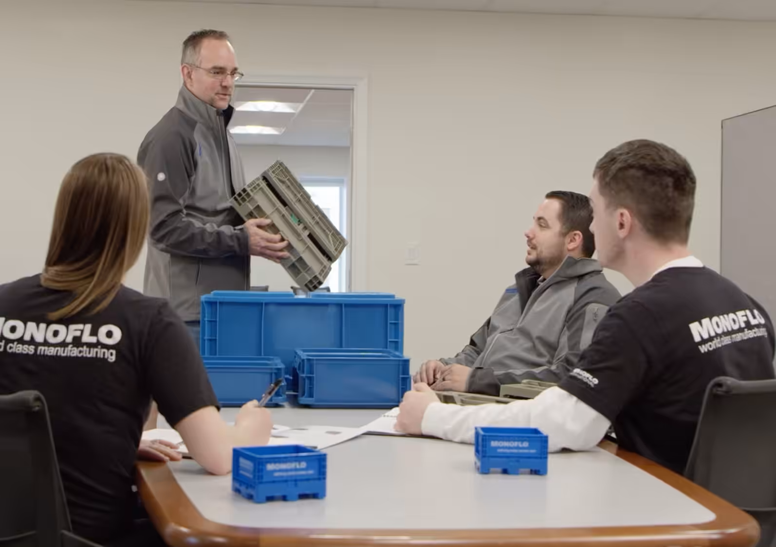 Team meeting in office as a presenter shows a plastic container model to coworkers seated around the table.