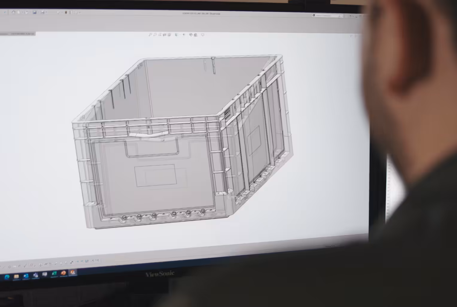 Engineer viewing a 3D CAD model of a plastic container on a computer screen.