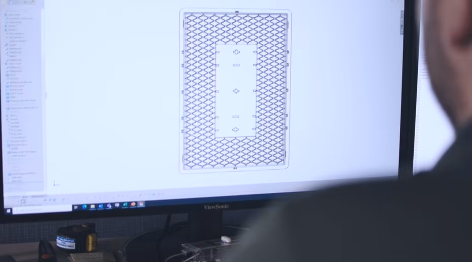 Engineer reviewing a CAD drawing of a rectangular plastic component with a grid pattern on a computer screen.