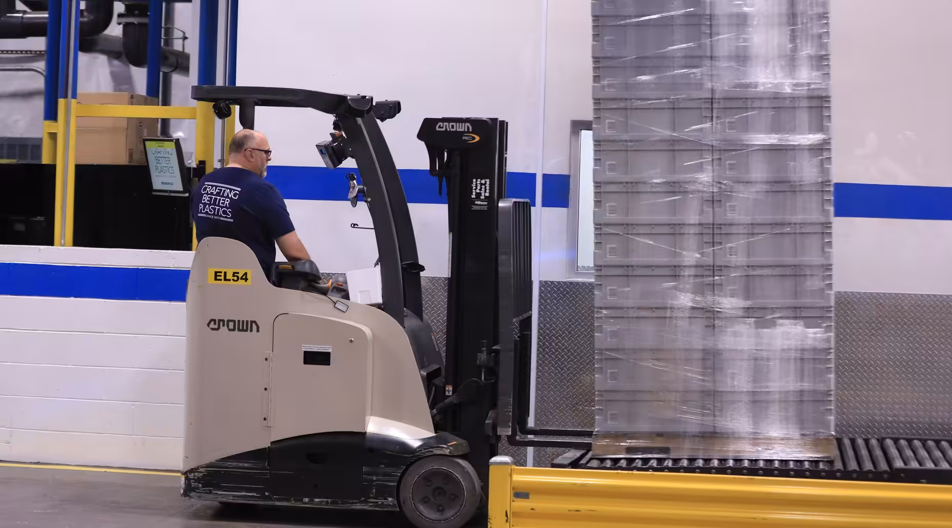 Worker operating a forklift to move a tall, shrink-wrapped stack of plastic containers inside a warehouse.