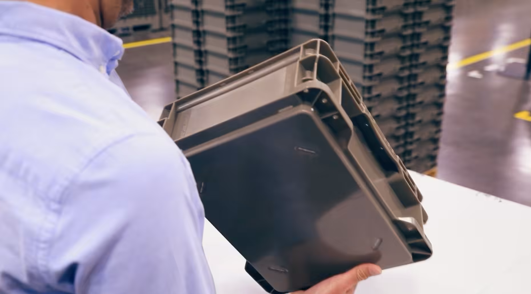 Person inspecting a gray plastic prototype container inside a manufacturing facility.