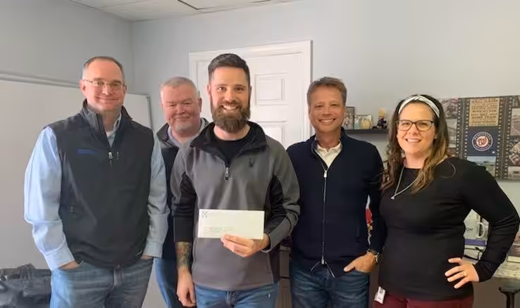 Five individuals in a room proudly holding a large check for Monoflo International's support of the Winchester Rescue Mission 2020.