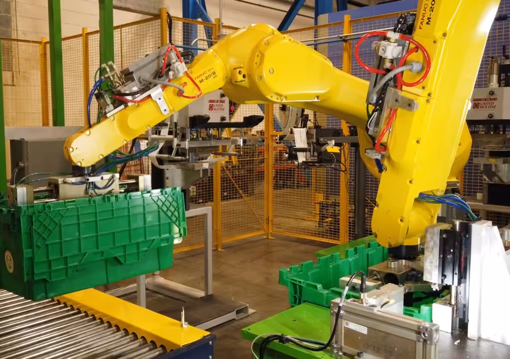 Yellow industrial robotic arm moving green plastic crates on a conveyor inside a fenced manufacturing cell.