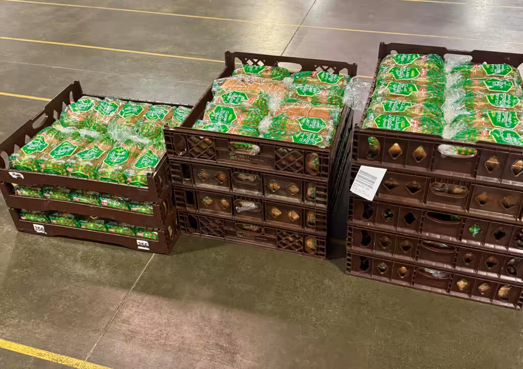 Stacks of plastic bakery crates filled with packaged bread loaves on a warehouse floor, ready for distribution.