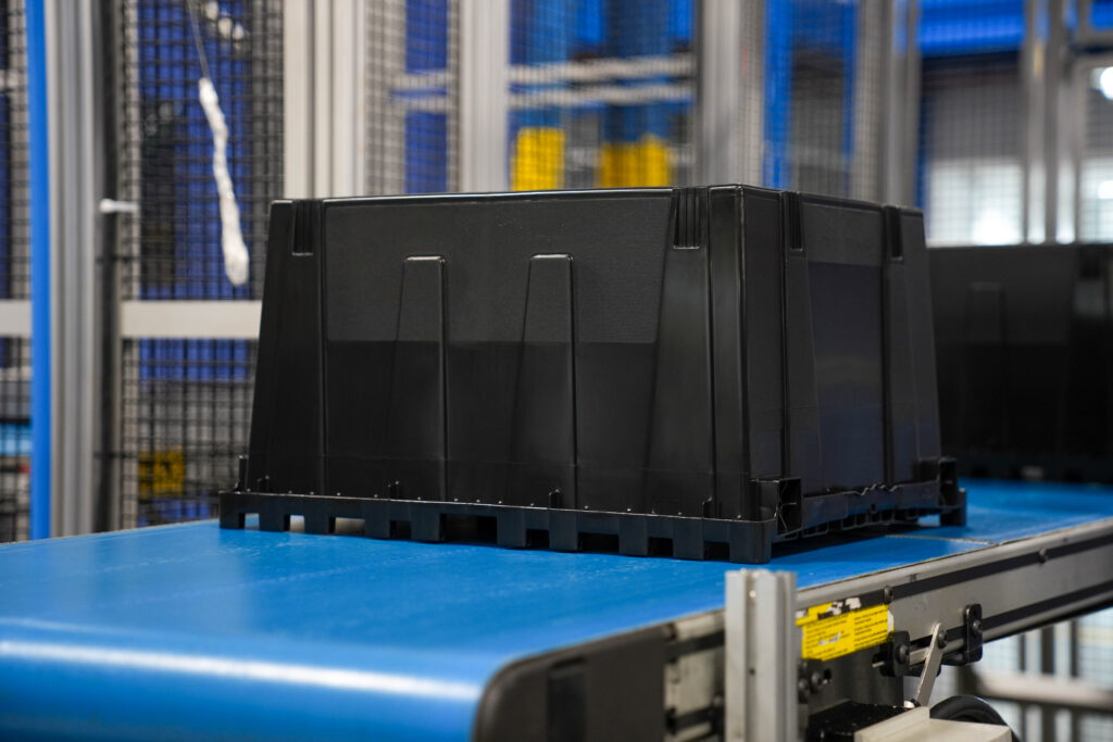 Black bin on conveyor belt in a production facility.